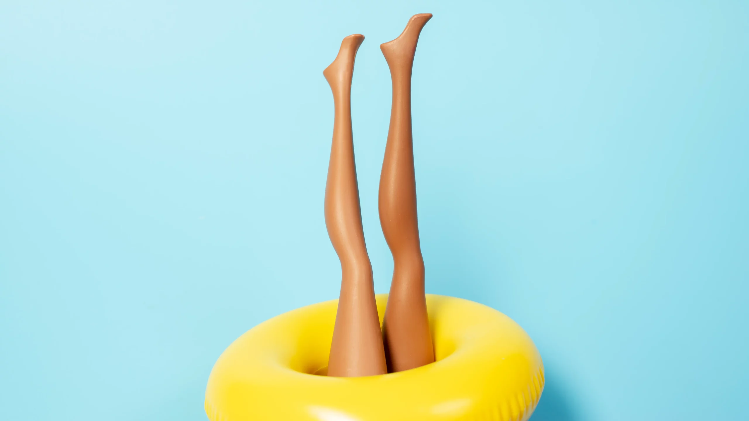 Lektorat Masterarbeit – Klarheit statt Kopfchaos Zwei Puppenbeine stecken kopfüber in einem Schwimmreifen – Symbol für den Zustand vor dem Lektorat der Masterarbeit