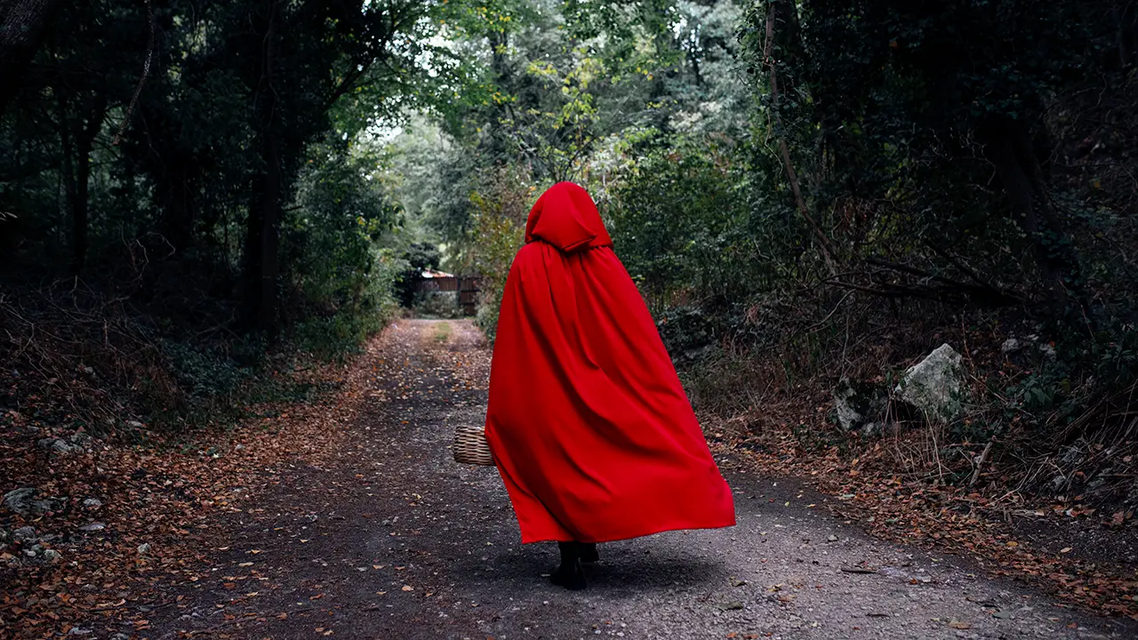 Person mit rotem Umhang auf einem Waldweg als Symbol für Märchen- und Fantasygeschichten im Buchlektorat