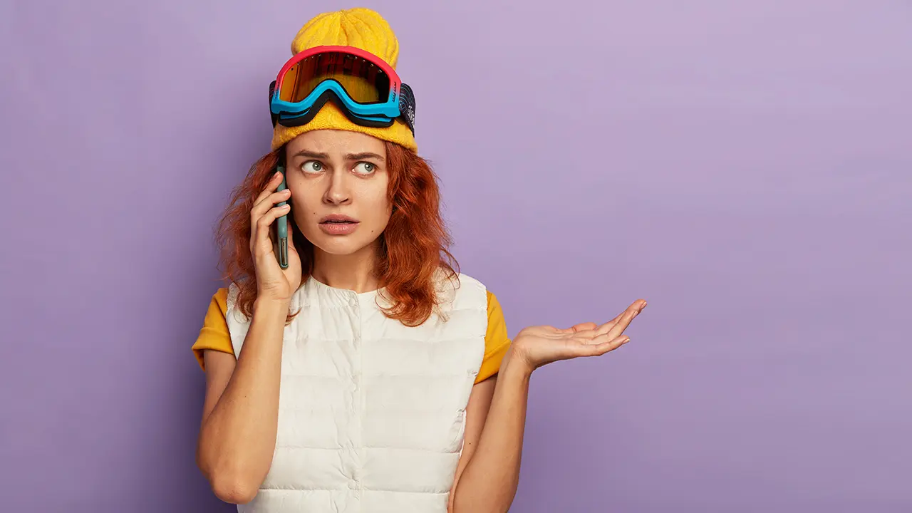 Textübersetzer für klare Kommunikation – Missverständnisse vermeiden, Botschaften treffen. Frau mit Skibrille und gelber Mütze schaut verwirrt beim Telefonieren – symbolisch für Kommunikationsprobleme, die ein Textübersetzer löst.