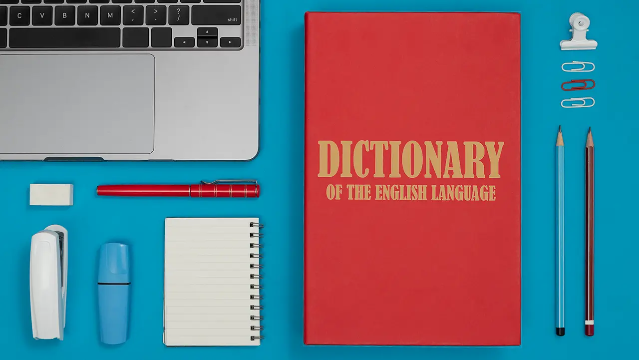 Übersetzer Englisch Deutsch – professionelle Sprachdienstleistungen mit Präzision und Stil. Laptop, Wörterbuch und Schreibutensilien auf blauem Hintergrund – Symbol für professionellen Übersetzer Englisch Deutsch.
